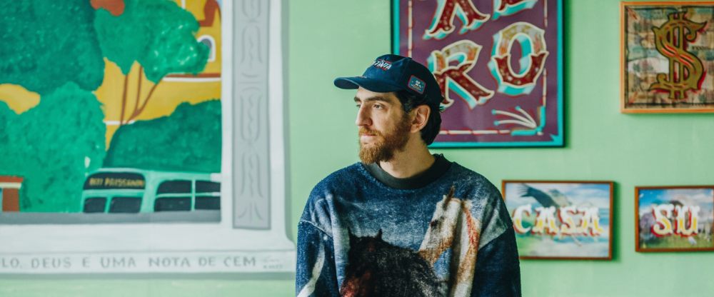 Retrato de Filipe Grimaldi entre letreiros pintados à mão, observando a paisagem urbana em entrevista e playlist para o deepbeep.